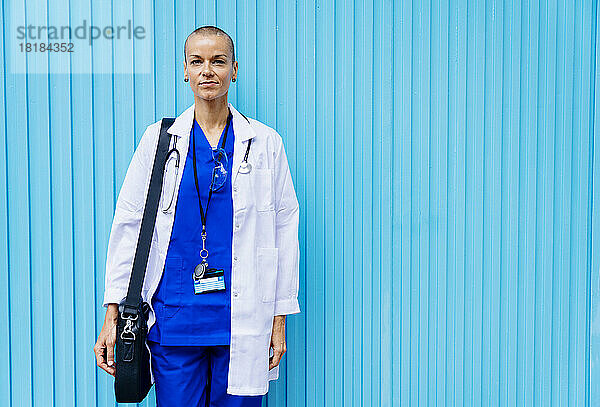 Reife Krankenschwester mit Umhängetasche vor einer blauen Wand