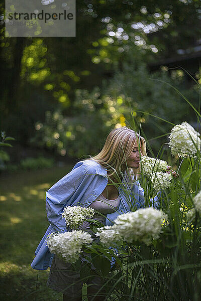 Reife Frau riecht Blumen im Garten