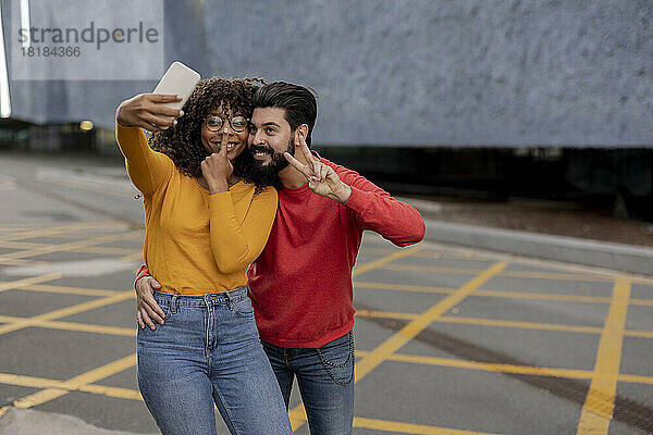 Glückliches junges Paar  das am Fußweg ein Selfie mit dem Smartphone macht