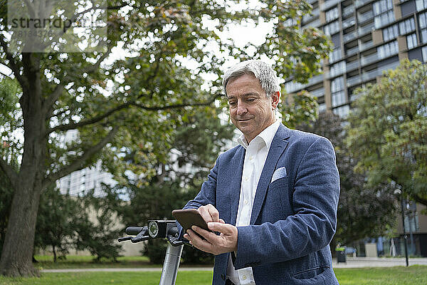 Reifer Geschäftsmann entsperrt Elektroroller per Smartphone