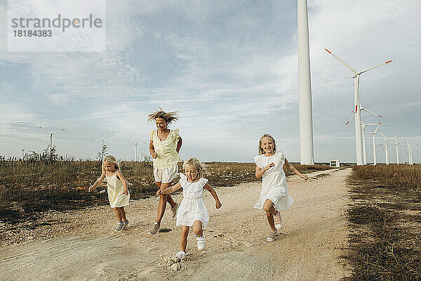 Glückliche Frau läuft mit Töchtern vor Windkraftanlagen