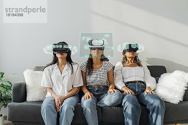 Friends wearing virtual reality glasses sitting on sofa at home