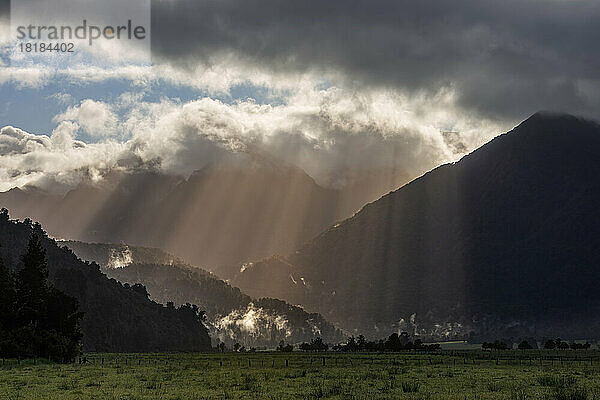 New Zealand  West Coast Region  Sunlight piercing through clouds floating over Southern Alps