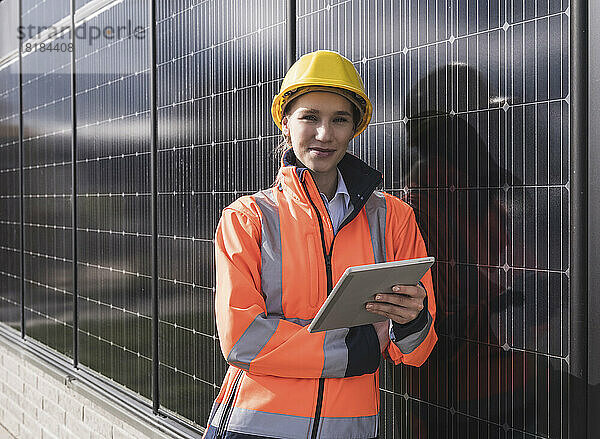 Lächelnde Ingenieurin mit Tablet-PC  der sich auf Sonnenkollektoren stützt