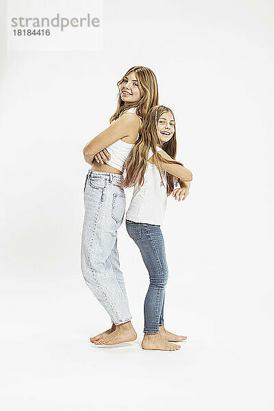 Smiling sisters standing with arms crossed together in studio