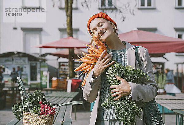 Lächelnde Frau umarmt ein Bündel Karotten auf dem Markt