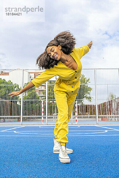 Glückliche Frau mit Afro-Frisur tanzt auf dem Basketballplatz