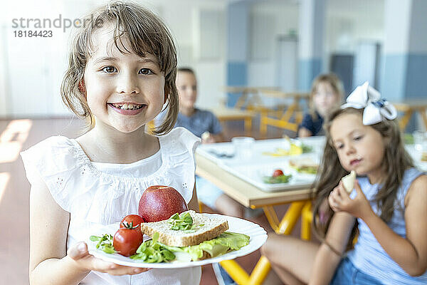 Lächelnder Student hält gesunde Mahlzeit auf dem Teller und steht in der Cafeteria