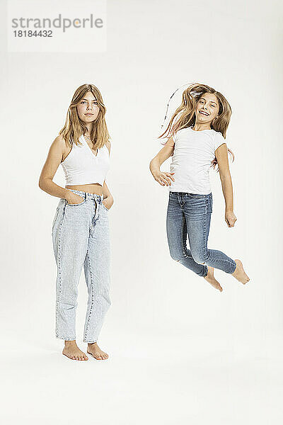 Confident teenage girl by sister jumping against white background