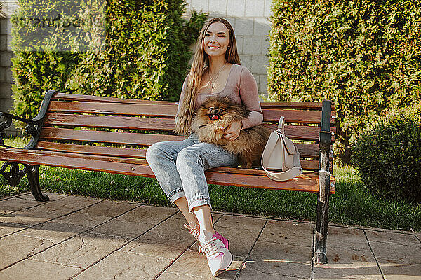 Lächelnde Frau mit Hund sitzt auf Bank im Park