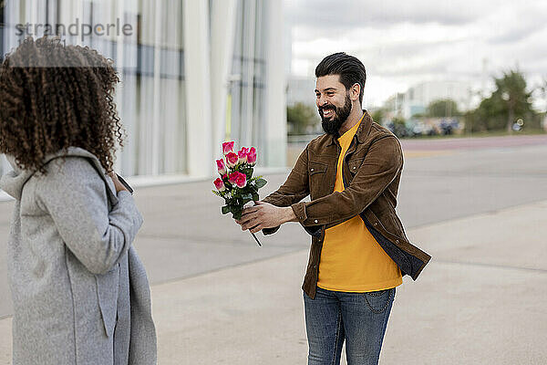 Glücklicher junger Mann schenkt Frau am Fußweg einen Blumenstrauß
