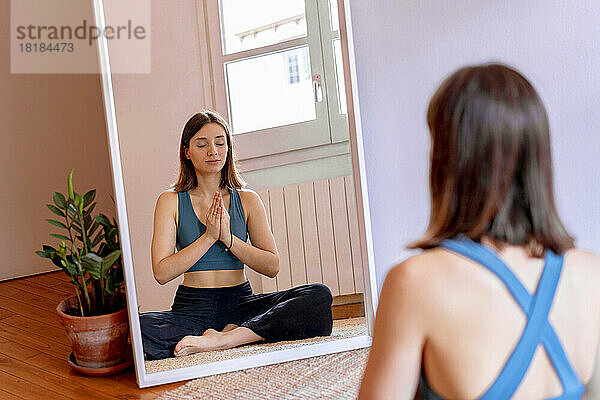 Junge Frau macht Yoga und reflektiert zu Hause im Spiegel