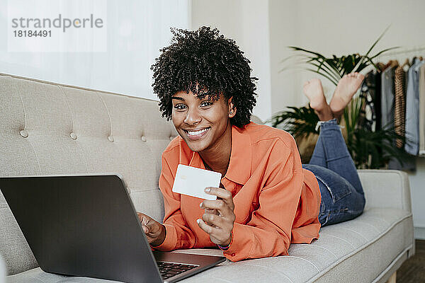 Glücklicher Freiberufler  der mit Laptop und Kreditkarte im Heimbüro auf dem Sofa liegt