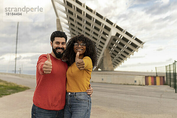 Glücklicher Mann mit Frau  die vor Sonnenkollektoren die Geste „Daumen hoch“ zeigt