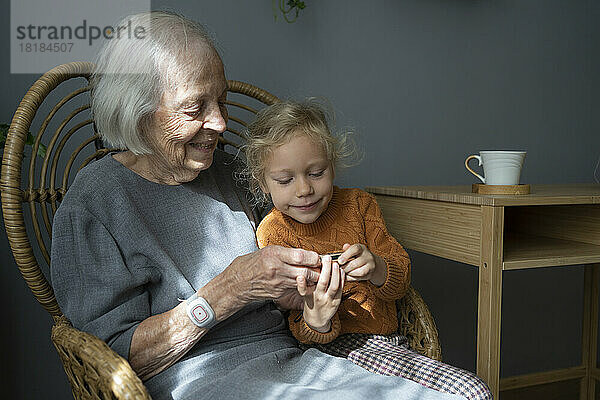 Glückliche Großmutter mit Enkelin  die auf einem Stuhl in die Kamera blickt