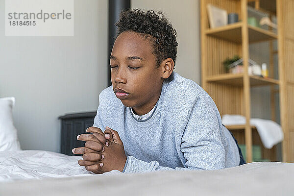 Boy with eyes closed praying by bed at home