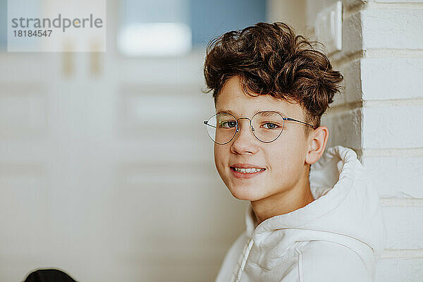Smiling boy wearing eyeglasses leaning on wall