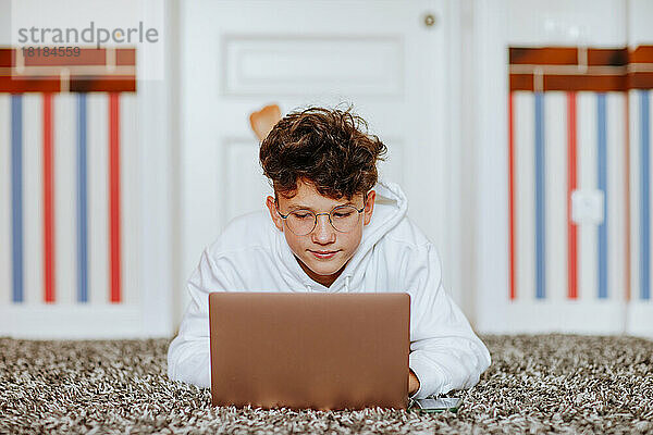 Junge liegt zu Hause mit Laptop auf Teppich