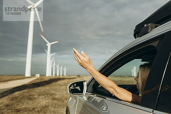 Frau sitzt mit erhobenem Arm aus dem Autofenster im Windpark