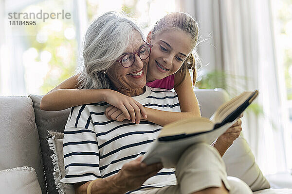 Großmutter liest Buch mit Enkelin auf Sofa zu Hause