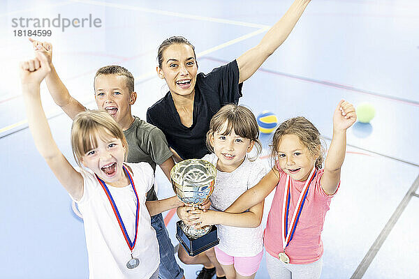 Lehrer feiert Sieg mit Schülern  die Trophäe auf dem Schulsportplatz halten