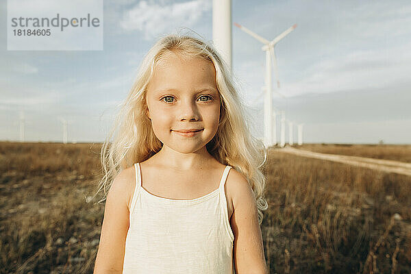 Nettes blondes Mädchen  das an einem sonnigen Tag im Windpark steht