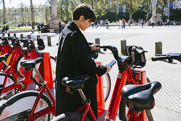 Frau mietet Fahrrad per Smartphone am Parkplatz