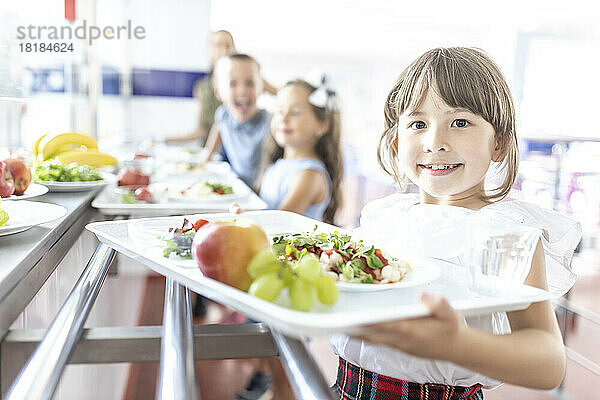 Smiling girl with food and fruits on tray at lunch break in cafeteria