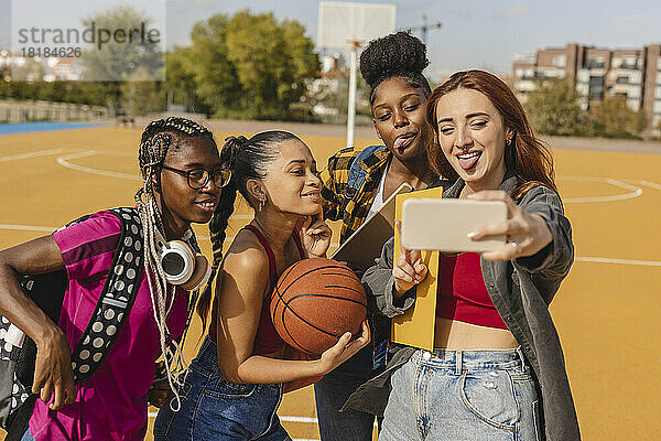 Glückliche junge Frau mit Freunden  die am Sportplatz ein Selfie per Smartphone machen