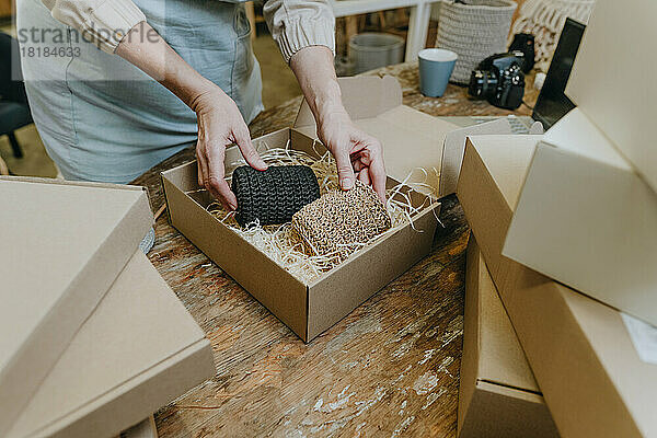 Hände einer reifen Handwerkerin  die Häkeldekor in einer Schachtel auf der Werkbank verpackt