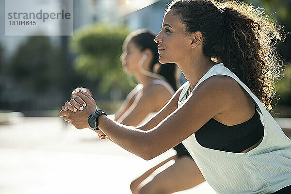 Smiling young woman with friend exercising on sunny day