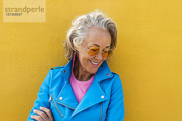 Lächelnde Frau mit Sonnenbrille vor gelber Wand