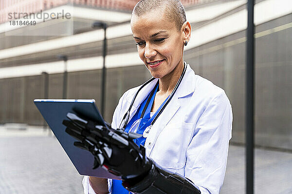 Lächelnder reifer Arzt  der einen Tablet-PC mit künstlicher Hand verwendet