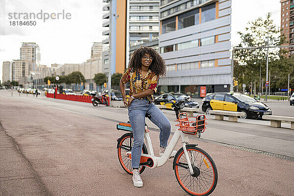 Lächelnde junge Frau sitzt auf dem Fahrrad am Fußweg