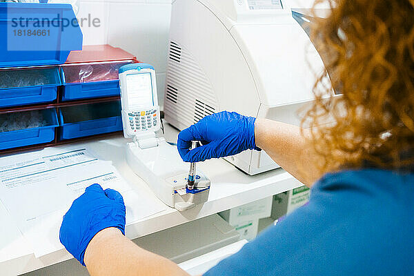 Reife Krankenschwester analysiert Blutprobe mit Geräten im Labor