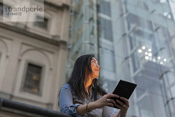 Nachdenkliche reife Frau hält Tablet-PC vor dem Gebäude