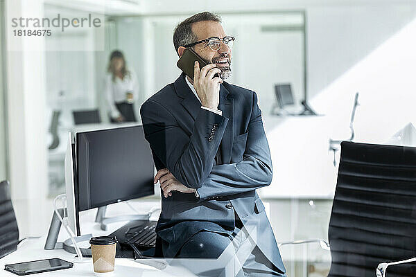 Lächelnder reifer Geschäftsmann  der im Büro mit dem Mobiltelefon spricht