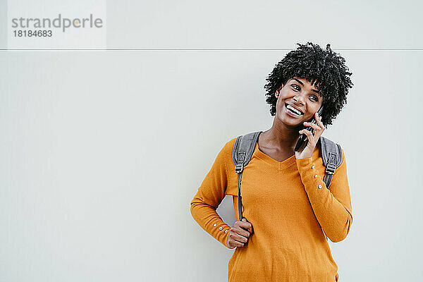 Glückliche junge Frau  die vor der Wand mit dem Handy spricht