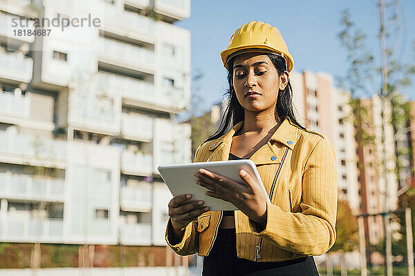 Woman wearing hardhat using tablet PC in front of buildings