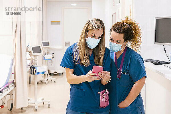 Krankenschwester trägt Maske und teilt Smartphone mit Kollegen im Krankenhaus