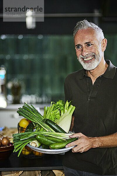 Glücklicher Mann steht mit Gemüse in der Küche