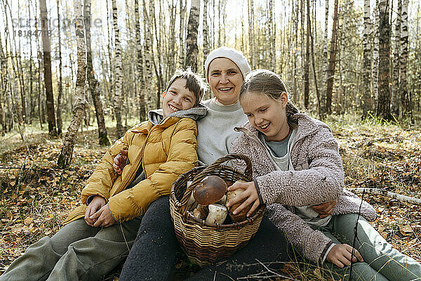 Lächelnde Großmutter  Junge und Mädchen sitzen mit einem Korb voller Pilze im Wald