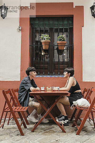 Lächelnder junger Mann im Gespräch mit Freundin im Straßencafé