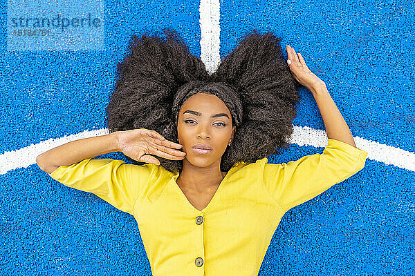 Woman with Afro hairstyle lying on blue basketball court