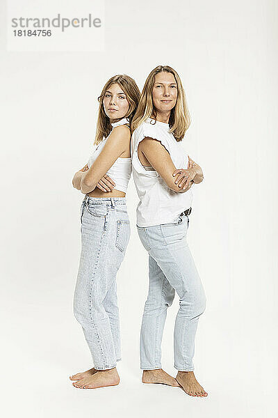 Confident mother and daughter standing with arms crossed in studio
