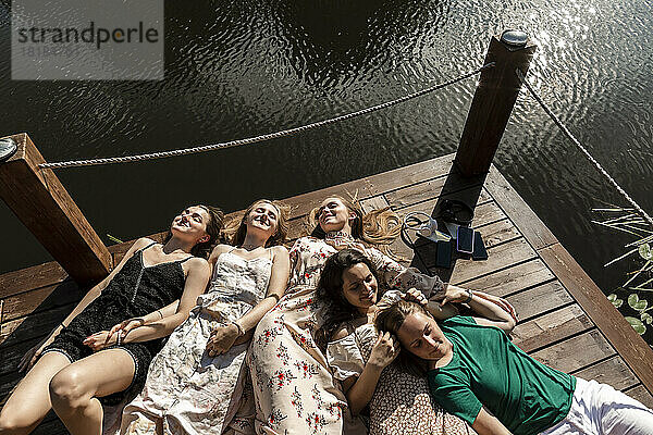 Smiling young friends with eyes closed lying on pier