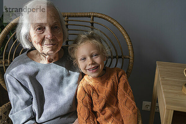Lächelnde ältere Frau mit Enkelin auf Stuhl zu Hause