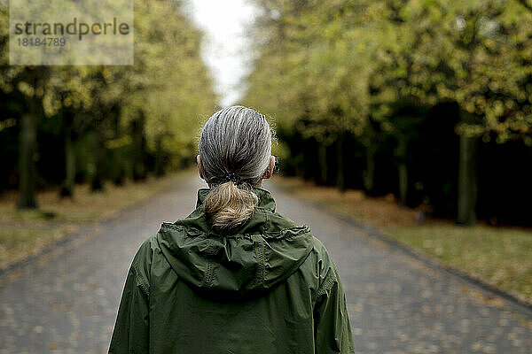 Ältere Frau mit grauem Haar trägt Regenmantel mit Kapuze