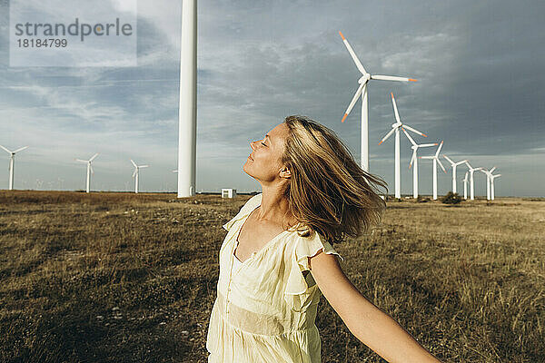 Sorglose Frau genießt es vor Windkraftanlagen auf dem Feld