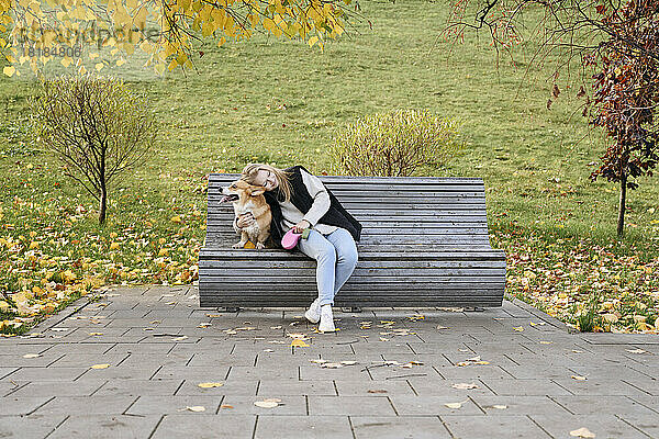 Frau umarmt Pembroke Welsh Corgi auf Parkbank